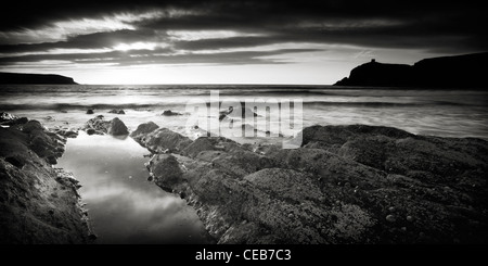 Vista sul mare da una spiaggia rocciosa. La marea ha lasciato una piscina nelle rocce che sta riflettendo la luce bassa. Foto Stock