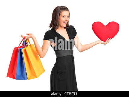 Un studio shot di una donna sorridente tenendo un cuore rosso Cuscino sagomato e shopping bags isolato su bianco Foto Stock