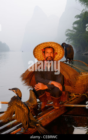 Cormorano pescatore in appoggio con uccelli su una zattera di bamboo sul fiume li carsico con picchi di montagna huangbutan cina Foto Stock