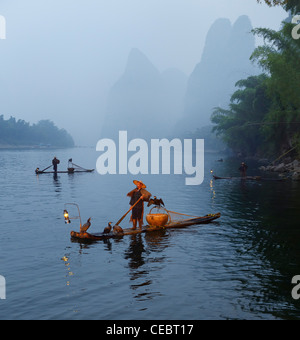 Cormorano pescatori nella nebbia all'alba sul fiume li carsico con picchi di montagna vicino xingping cina Foto Stock