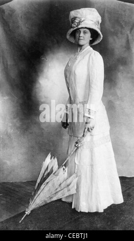 Donna che indossa piede-lungh.. abito e cappello e ombrello di contenimento con la punta sul pavimento.! Circa 1910 Foto Stock