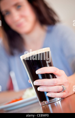 Giovane donna tenendo una pinta di birra con un pranzo in un pub Foto Stock