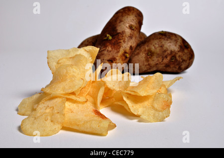 Un mucchio di patatine di sedersi su un semplice sfondo bianco con un paio di patate in background. Foto Stock