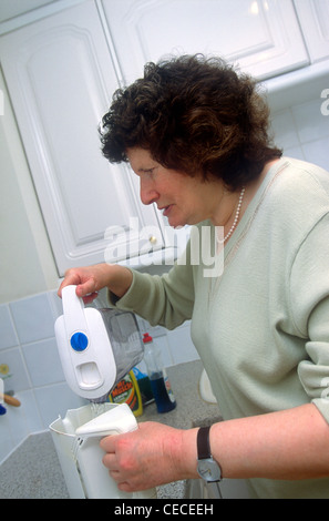 Ipovedenti donna il riempimento di un bollitore in cucina, Eastbourne, Sussex, Regno Unito. Foto Stock