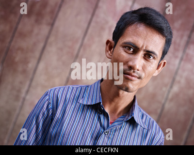 Ritratto di metà adulto uomo asiatico fissando la telecamera contro la parete marrone. Spazio di copia Foto Stock