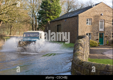 Allagamento - Land Rover Defender guidare & spruzzi attraverso le profonde acqua di inondazione su allagata strada rurale dopo la pioggia torrenziale - North Yorkshire, Inghilterra, Regno Unito Foto Stock
