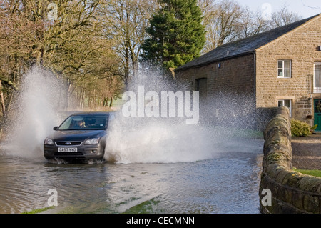 Allagamento - donna alla guida di auto nera & spruzzi attraverso le profonde acqua di inondazione su allagata strada rurale dopo la pioggia torrenziale - North Yorkshire, Inghilterra, Regno Unito. Foto Stock