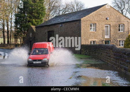 Inondazioni- uomo alla guida di furgone rosso, schizzi attraverso le profonde acqua di inondazione su allagata strada rurale (lane) dopo la pioggia torrenziale - North Yorkshire, Inghilterra, Regno Unito. Foto Stock