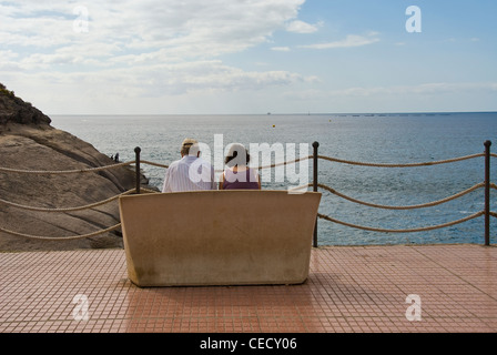 Coppia senior seduto su una panchina affacciata sul mare.Playa del Duque Foto Stock