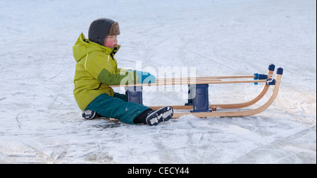 Piccolo Ragazzo freddo seduto sul ghiaccio con slitta Foto Stock