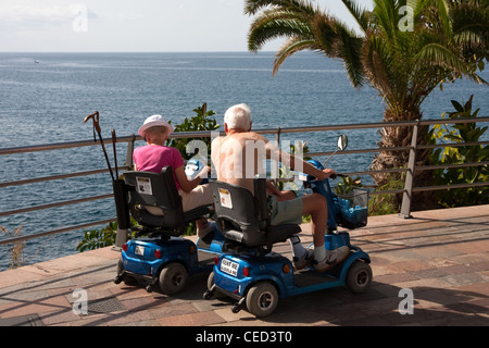 Coppia di anziani sulla mobilità scooter che guarda al mare Foto Stock