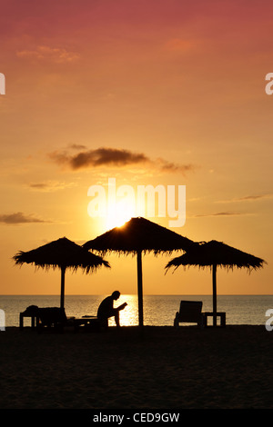 Persona la lettura di un libro sulla spiaggia al tramonto, silhouette, Kib Hotel, Koh Kho Khao Islanda, nel sud della Thailandia Foto Stock