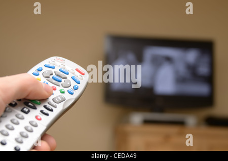 TTelevision remote in primo piano con il fuoco selettivo e la televisione in background. Foto Stock