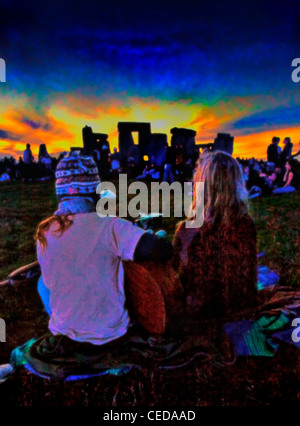 Una giovane coppia hippy guardare il tramonto mentre suonando la chitarra a Stonehenge Solstizio d'estate Festival Foto Stock