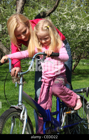 Madre impara la figlia ad andare in bicicletta nel giardino di primavera Foto Stock