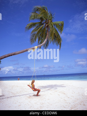 Giovane donna seduta al di sotto di palma, Kuda Bandos, Kaafu Atoll, Repubblica delle Maldive Foto Stock