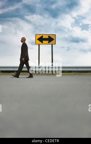 African American businessman camminando sulla strada vicino al cartello stradale Foto Stock