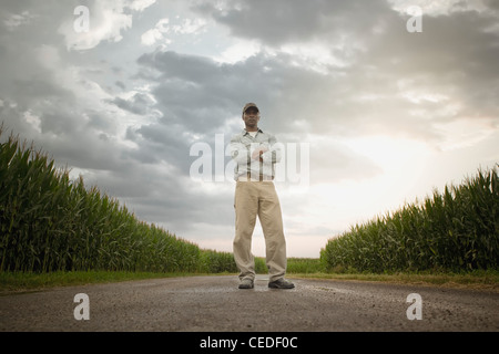 African American Farmer permanente sulla strada attraverso le colture Foto Stock