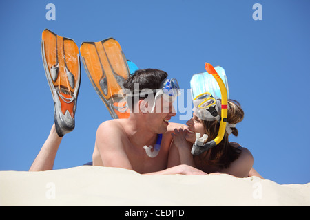 Giovane coppia di alette e le maschere subacquee giace sulla sabbia Foto Stock
