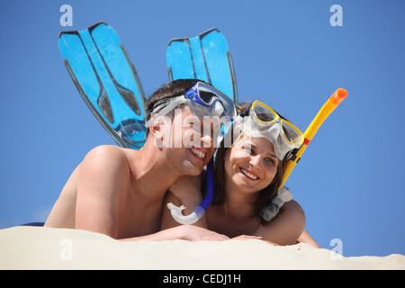 Giovane coppia di alette e le maschere subacquee giace sulla sabbia Foto Stock
