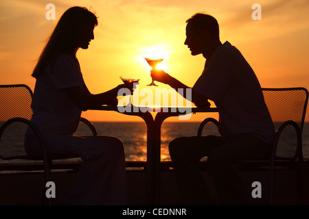 Donna e uomo di sagome su sunset sedere al tavolo con due bicchieri per esterno Foto Stock
