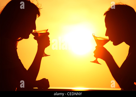 Donna e uomo di sagome su sunset bere da bicchieri Foto Stock