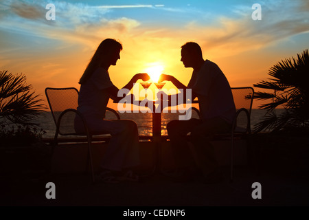 Donna e uomo di sagome su sunset sedere al tavolo con due bicchieri per esterno Foto Stock