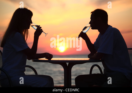Donna e uomo di sagome sul tramonto dietro la tabella da Bere bicchieri, concentrarsi sull'uomo Foto Stock