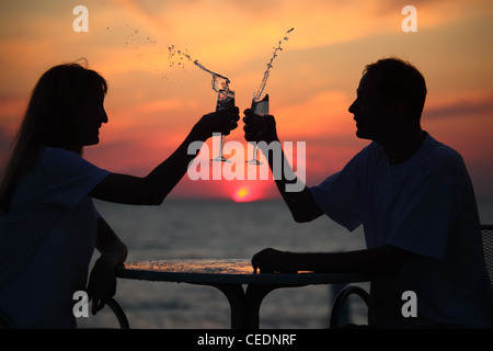 Sagome di uomo e donna schizzare fuori dal bere dal bicchiere sul mare tramonto. focalizzazione sull'uomo Foto Stock