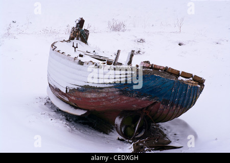 Vecchio legno stagionato barca da pesca Spiaggiata sulla coperta di neve Riverbank UK Winter Foto Stock