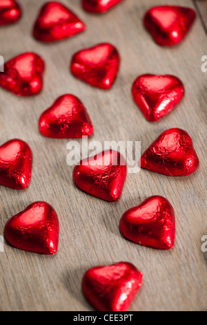 Il cioccolato a forma di cuore le caramelle confezionate in lamina rossa seduta sul pavimento in legno Foto Stock