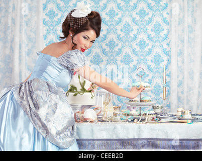 Licenza e stampe a MaximImages.com - bella donna asiatica in un abito blu fantasia a una festa del tè con un tavolo di festa Foto Stock