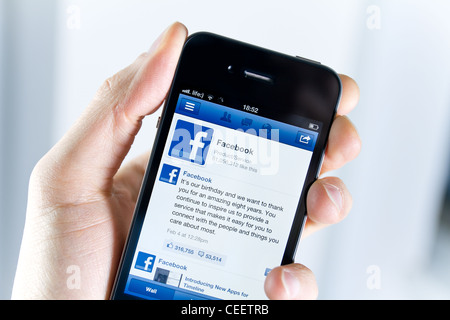 Un uomo azienda Apple iPhone 4 con un'applicazione Facebook sullo schermo. Foto Stock