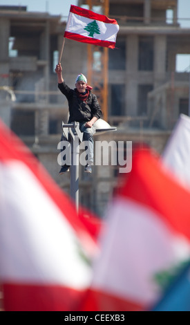 Giovani libanesi uomo sulla cima di streetlamp bandiera onde alte come massa politica dei rally in Piazza Martiri, Beirut, Libano. Bandiere in primo piano Foto Stock