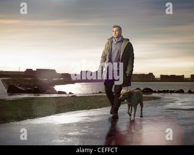 Uomo che cammina cane sulla strada bagnata Foto Stock