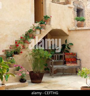 Panca in legno sulla piccola terrazza pavimentata di Majorcan tradizionale casa con la fioritura di piante in vaso sui gradini esterni Foto Stock