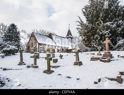 San Nicola, Chiesa Hill, Pyrford, Surrey in Inghilterra con grave lapidi e croci nel cimitero, nella neve Foto Stock