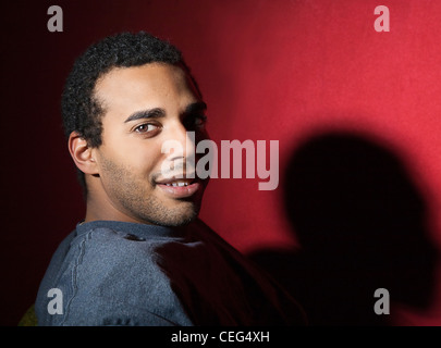 Giovane maschio afro-americano, la testa girata a guardare la fotocamera. Colpo di testa contro uno sfondo di colore rosso. Foto Stock