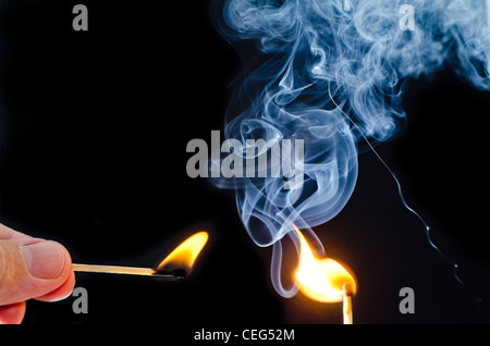 Illuminazione uomo una corrispondenza con un altro match, con fumo blu rising contro uno sfondo nero. Foto Stock