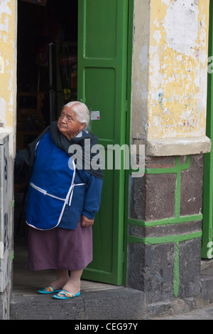 Un'anziana donna indigena si trova in un portale guardando giù per la strada di Latacunga, Ecuador. Foto Stock