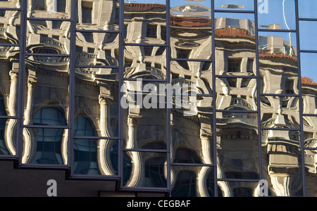 Distorto i riflessi di un edificio in stile neoclassico si riflette nelle finestre di un vetro moderno alto edificio. Foto Stock