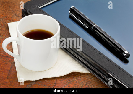 Tazza di caffè espresso, penna e tavoletta computer nella custodia in pelle nera su un legno di grunge Foto Stock