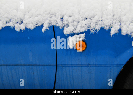 Auto blu coperto di neve. Dettaglio del lato luci ad intermittenza in piedi fuori dalla porta blu sotto la neve. Foto Stock