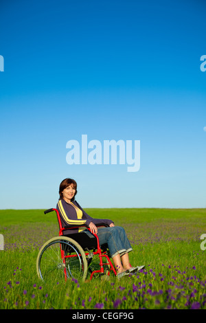 Donna disabile su sedia a rotelle sorridente su un verde prato Foto Stock