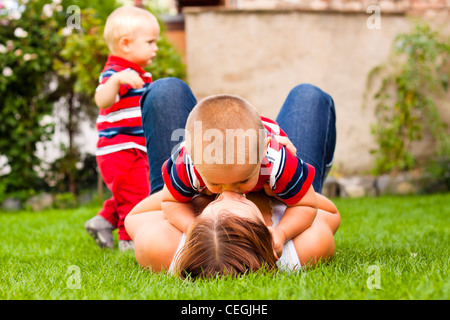 Felice madre baciare il figlio suo rilassante sull'erba nel giardino. Foto Stock