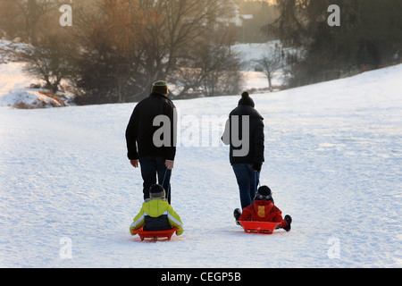 Torna alla vista della telecamera di una famiglia tirando toboggans attraverso la neve. Foto Stock