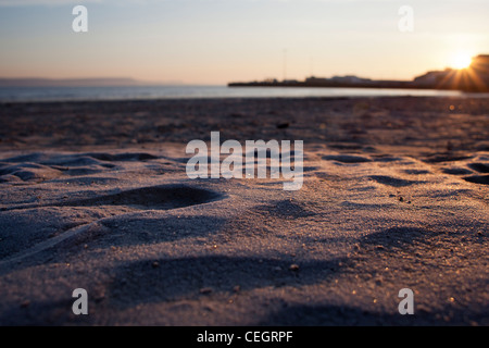 La brina sulla spiaggia di Weymouth come sole sorge sulla baia. Foto Stock