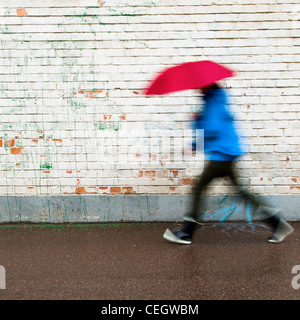 Persona a piedi sotto la pioggia con ombrello Foto Stock