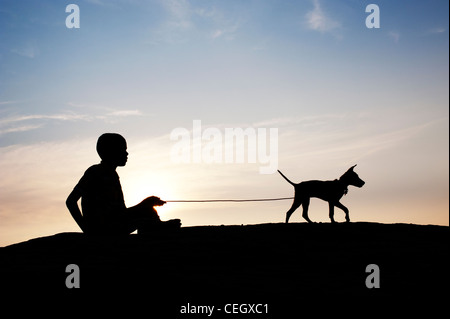 Silhouette di un giovane ragazzo indiano seduto e giocare con il suo cucciolo. India Foto Stock