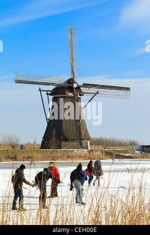 Tipicamente olandese scena mostrando persone il pattinaggio su ghiaccio naturale con i mulini a vento di Kinderdijk come sfondo. Foto Stock